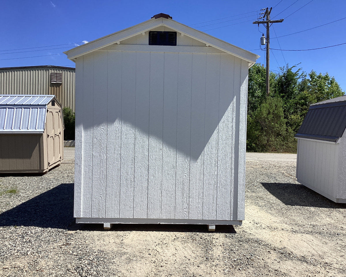 Small storage shed with a white exterior and black roof in an outdoor setting.